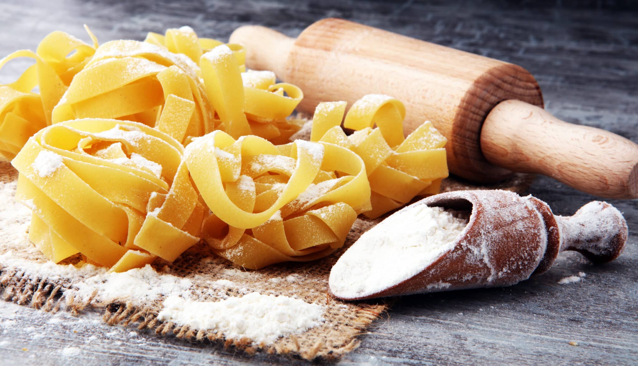Making homemade pasta linguine on rustic kitchen table with flour, rolling pin and pasta
