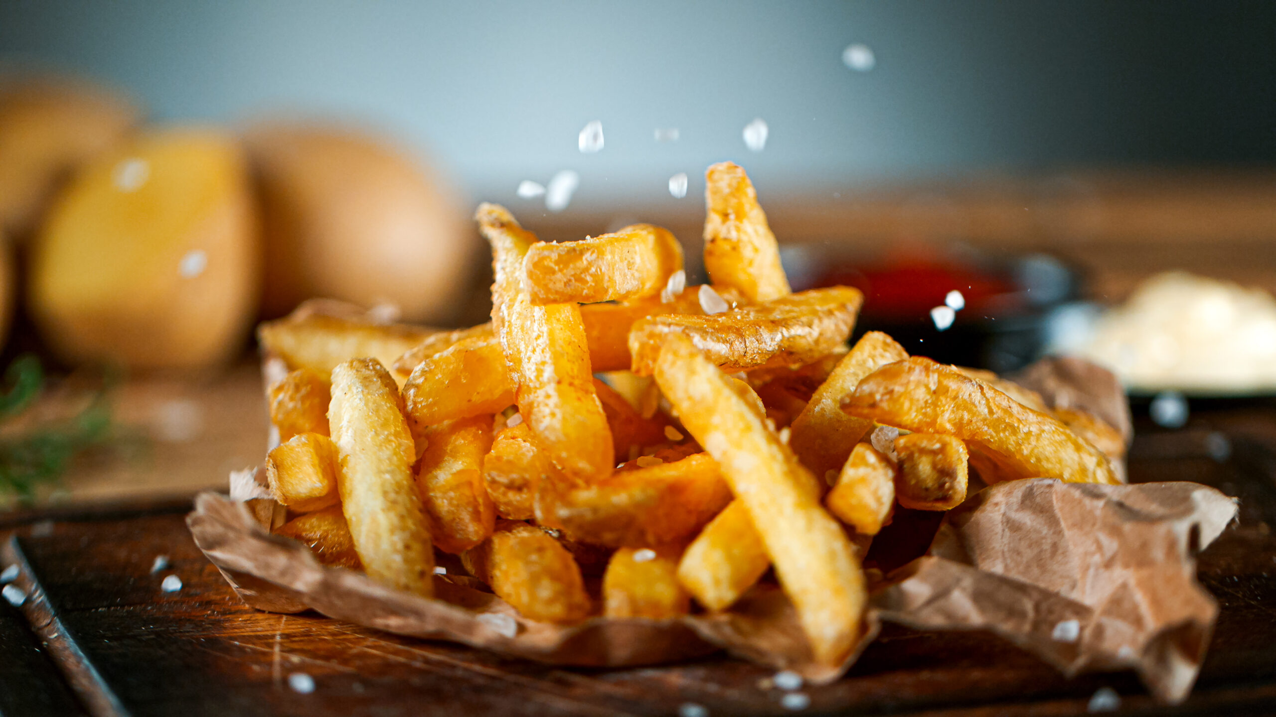 Shot of Falling Fresh French Fries on Wooden Table